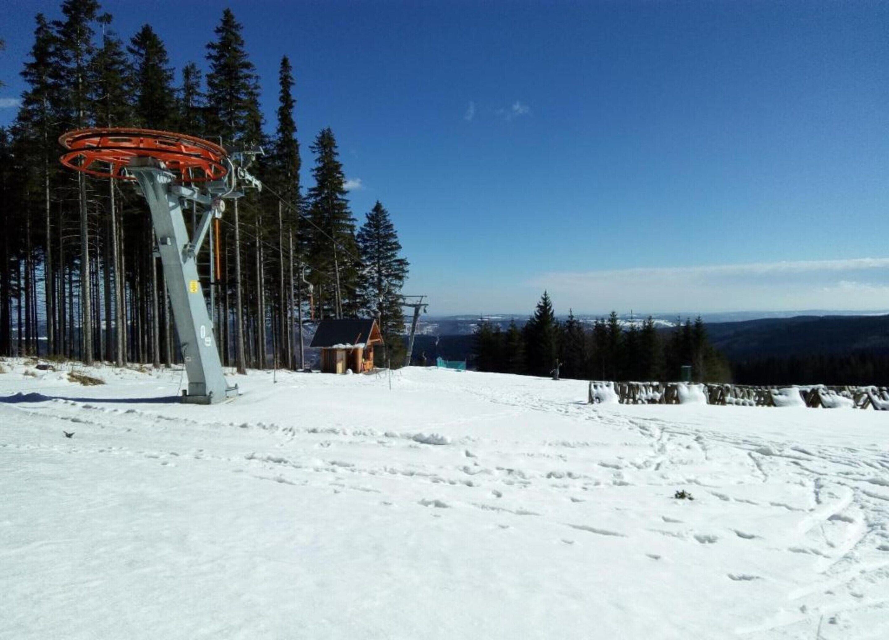 A ski lift with a cabin and a chairlift, surrounded by snow-covered ground and tall trees.
