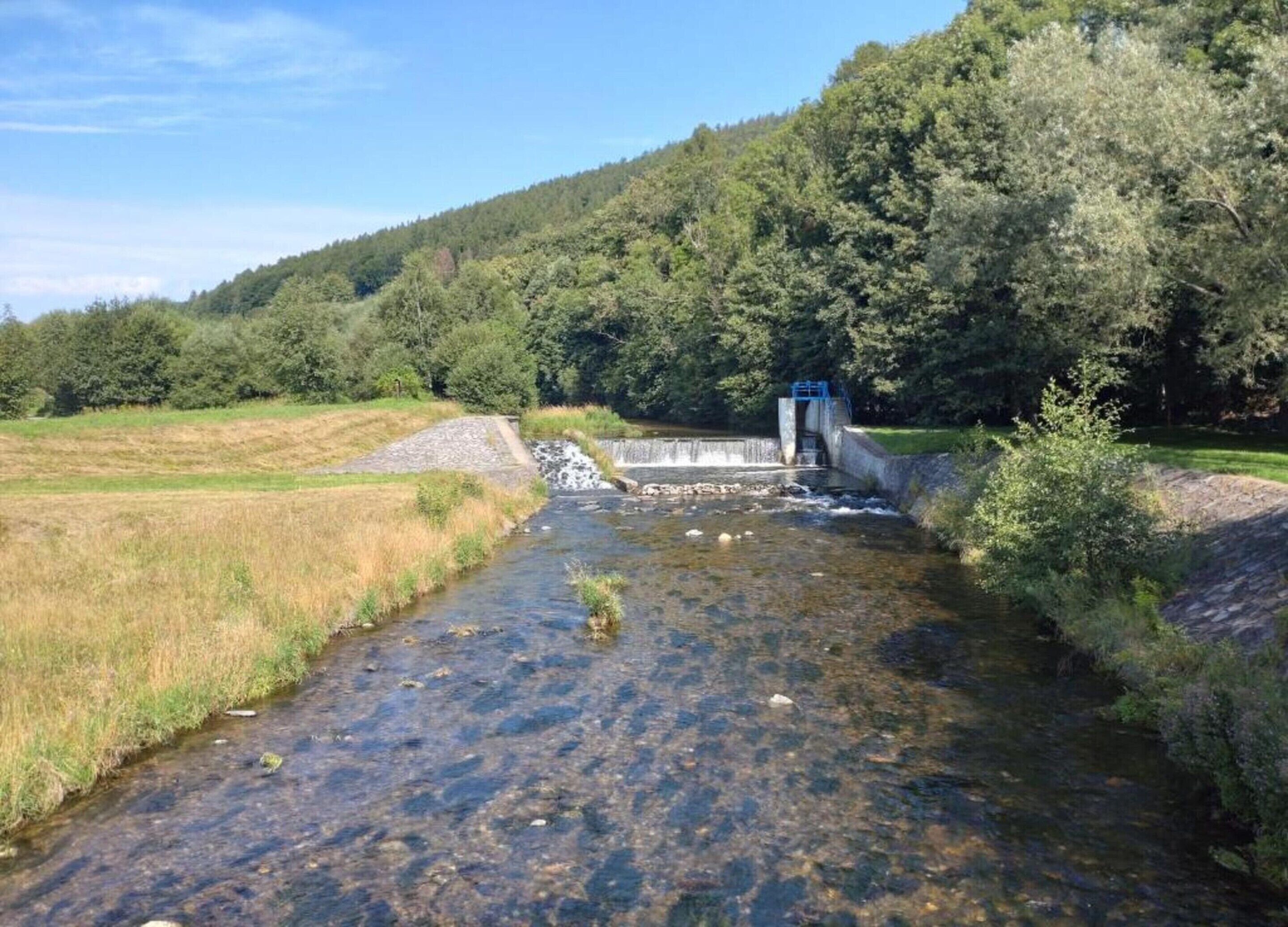 A river flowing through a natural landscape with a small bridge and a dam.