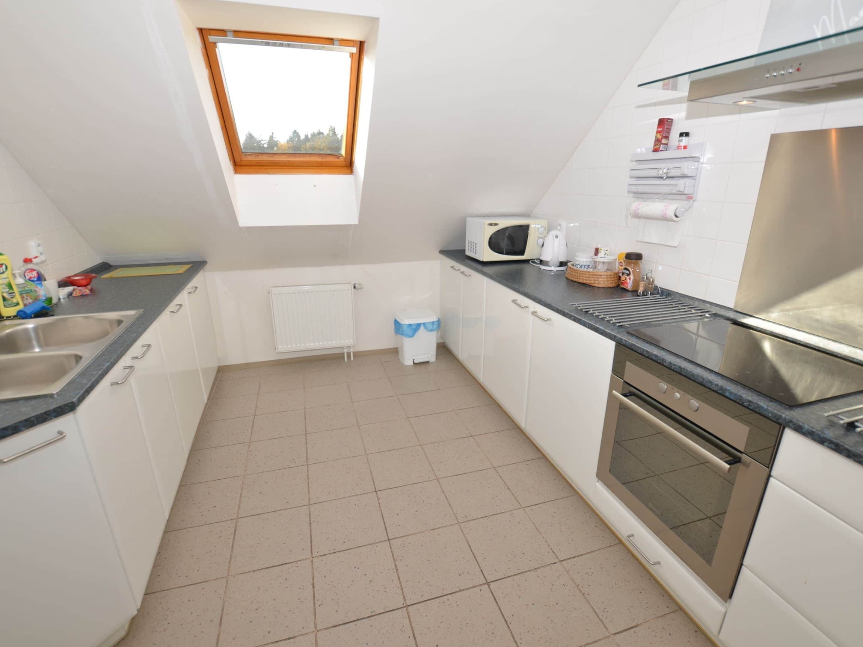 A compact kitchen with a window, white cabinets, a microwave, a kettle, and a stainless steel oven.