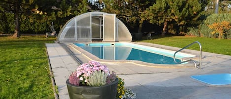 A swimming pool with a glass enclosure, surrounded by a paved deck and a grassy area.