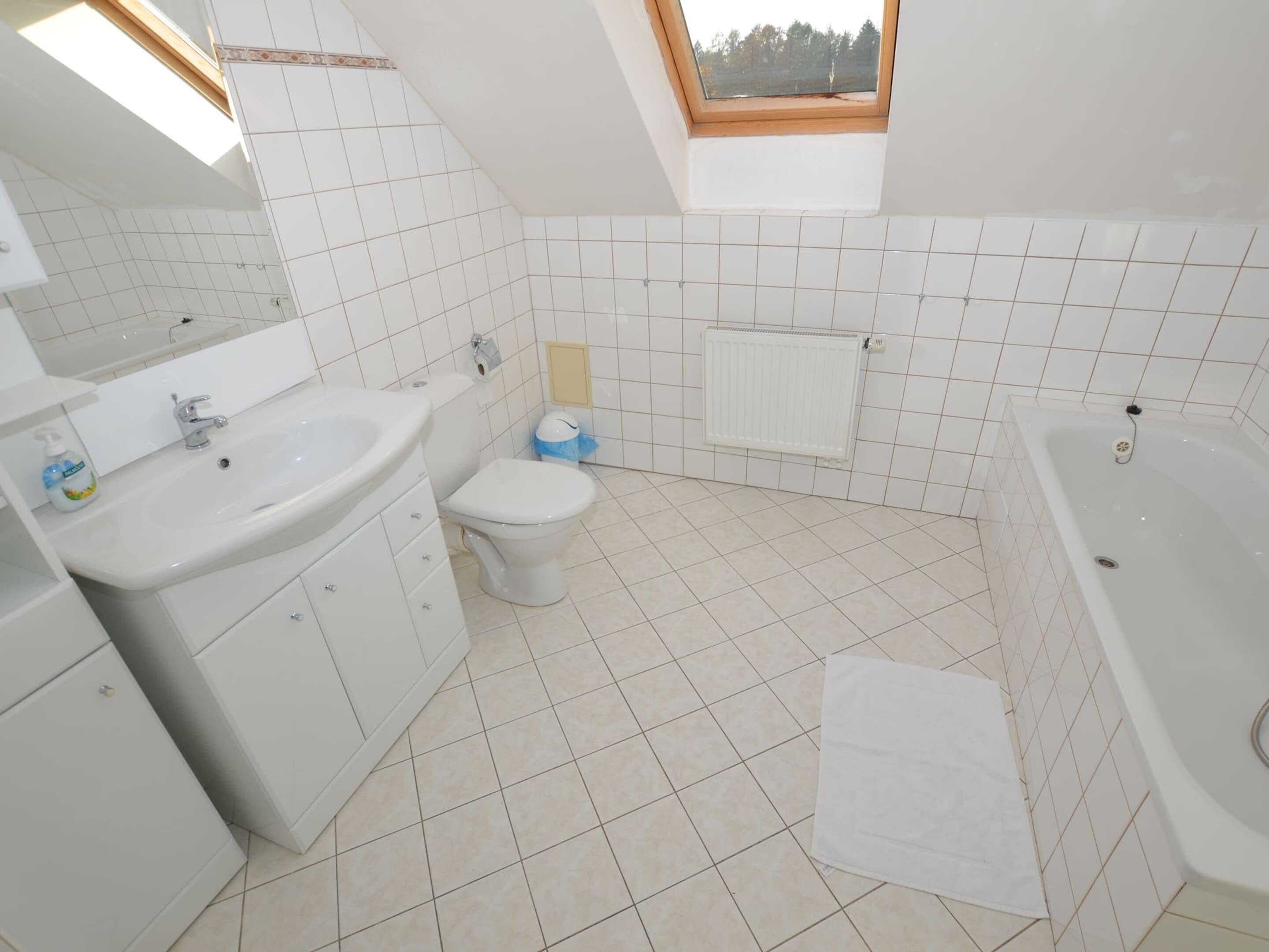 Un baño moderno con tragaluz, azulejos blancos, lavamanos, inodoro y bañera.