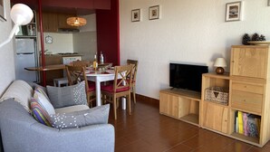 Un espace de vie compact comprenant un canapé gris, une table à manger en bois et un téléviseur posé sur un meuble en bois.