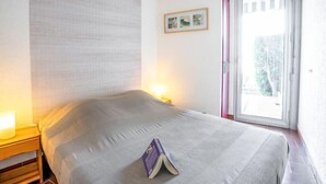 Une chambre d’hôtel avec un lit, une table de chevet avec une lampe, une fenêtre donnant sur des arbres et un tableau encadré au mur.
