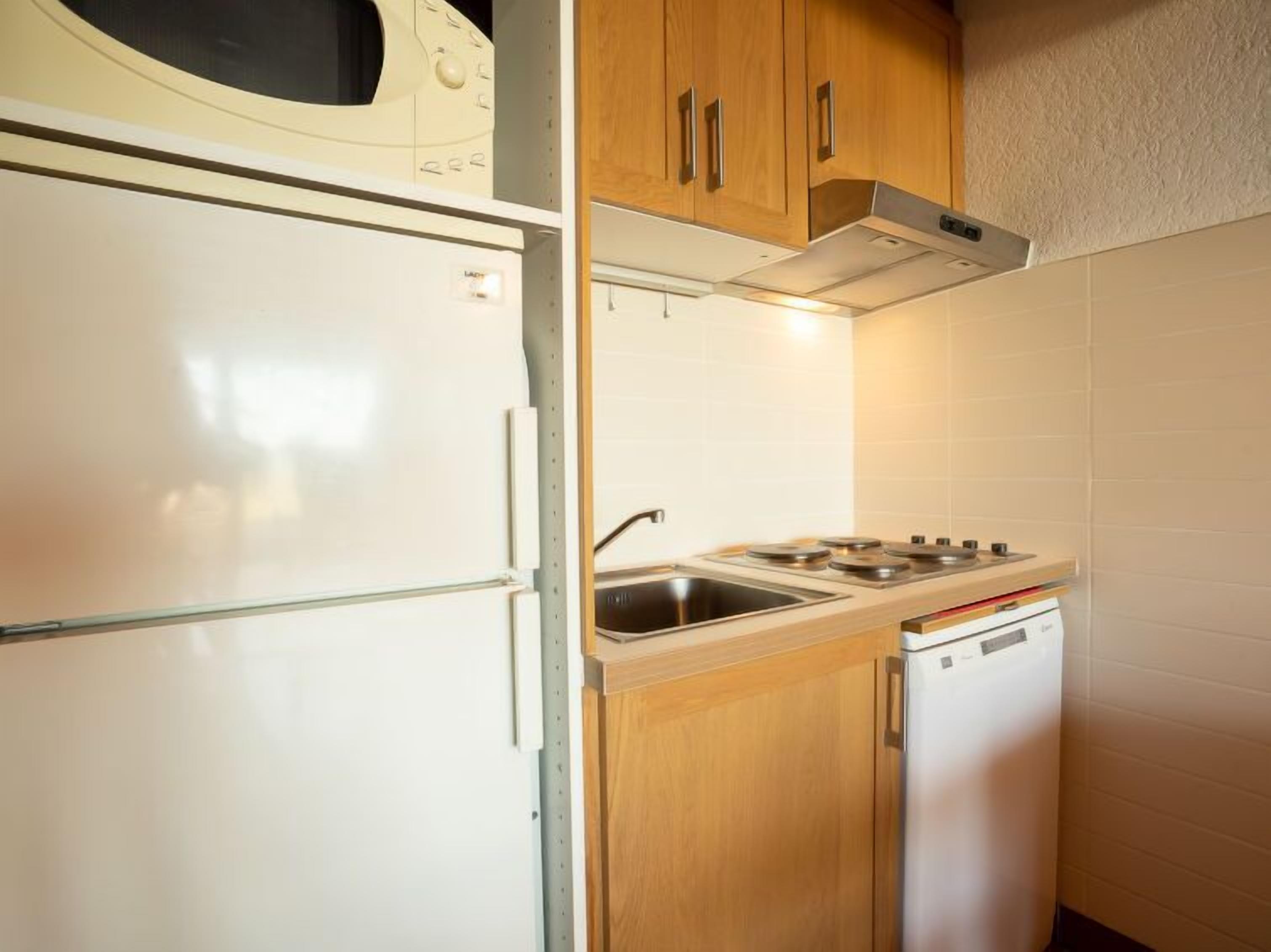 Pieni, käytännöllinen keittiö, jossa on valkoinen jääkaappi, mikroaaltouuni, liesi ja astianpesukone.
