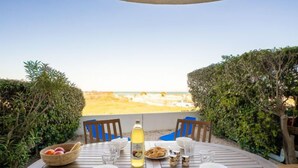 Une table ronde en bois, entourée de chaises, avec une bouteille de boisson et une assiette de nourriture, le tout placé de manière à offrir une vue sur la plage.