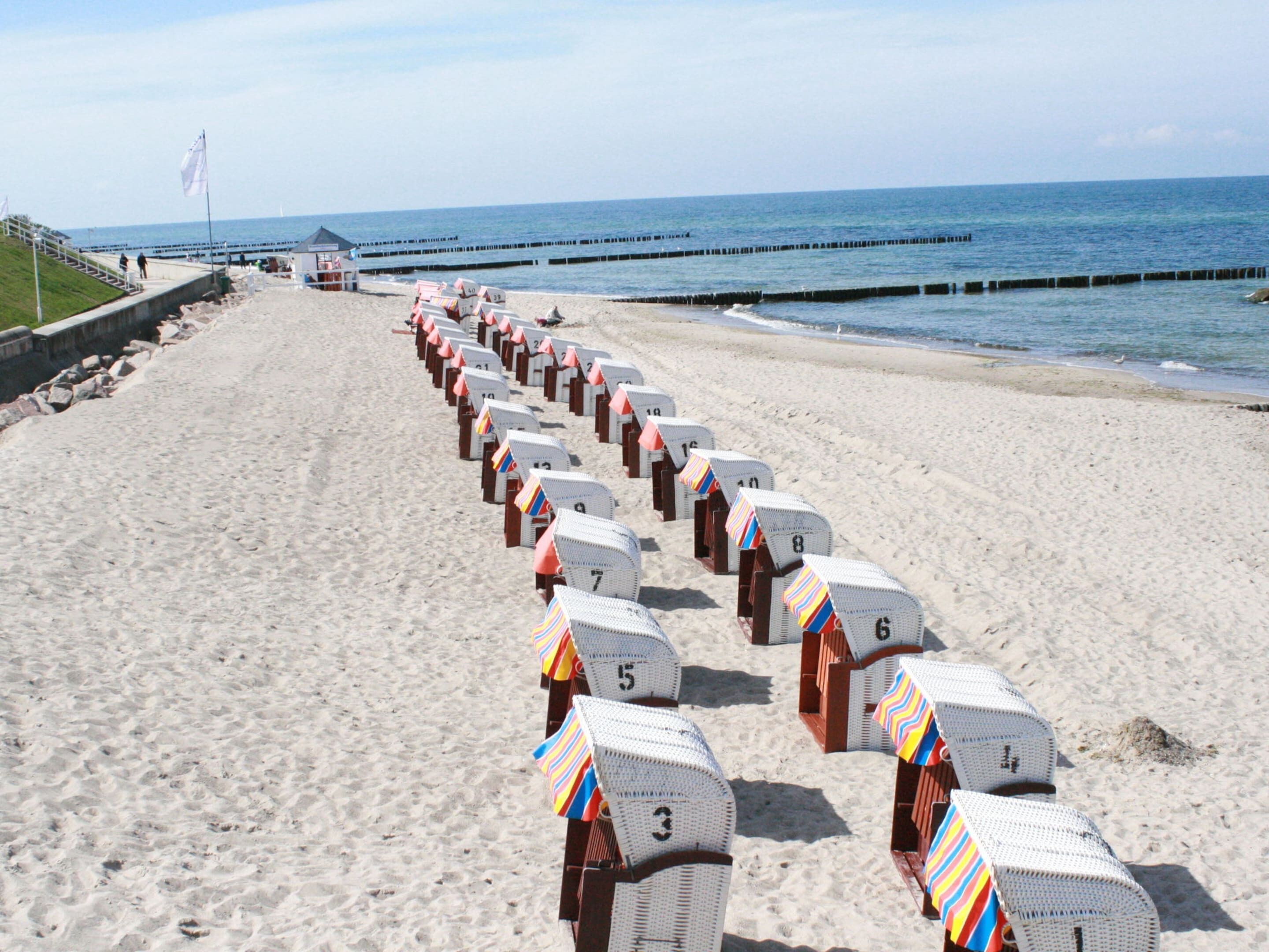 A beach with rows of numbered beach huts along the shoreline.