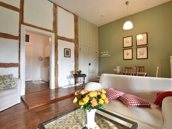 A living room with a white sofa, a wooden floor, a green wall with framed pictures, and a hanging light fixture. - Wohnung Nahe Ostsee Kuhlungsborn (Satow)