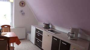 A compact kitchen with a dining table, chairs, a coffee maker, and a clock on the wall. - Restful Apartment in Neukloster Germany near Lake (Neukloster)
