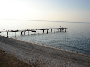 A pier extending into calm waters with a pebbled beach in the foreground.