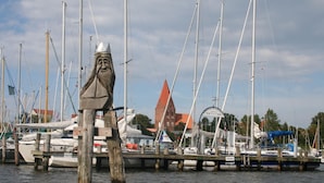 A marina with boats docked, a wooden post in the foreground, and a building with a red roof in the background.