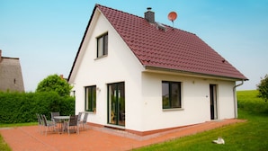 A single-story house with a red-tiled roof, a satellite dish, and a patio with a table and chairs.
