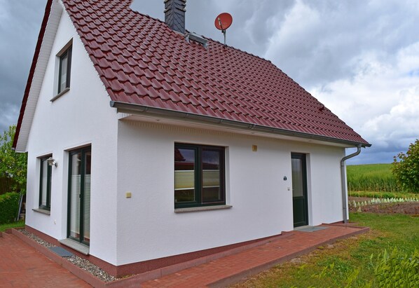 Une maison de plain-pied avec un toit recouvert de tuiles rouges, des murs extérieurs blancs et un petit porche à l’avant.