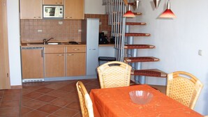 A compact kitchen with wooden cabinets, a microwave, and a refrigerator. There is a dining area with a table and chairs, and a staircase with a railing. - Wohnung mit Balkon in Zingst Deutschland (Zingst)