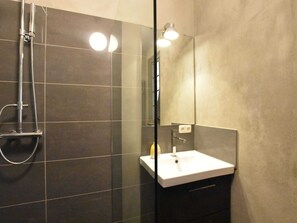 Ein modernes Badezimmer mit einer Glaskabine, einem weißen Waschbecken und einem Spiegel.