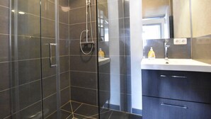 Ein modernes Badezimmer mit einer in Glas abgeschlossenen Dusche, einem weißen Waschbecken und dunklen Schränken.