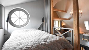Une chambre à coucher avec un lit, une fenêtre ronde, un bureau et un escalier.