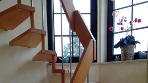 Eine hölzerne Wendeltreppe mit Metallgeländer, die zu einer Zwischenebene mit einem Fenster führt.
