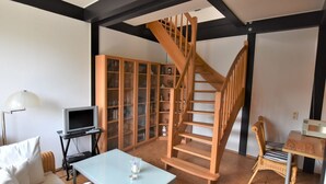 A living room with a glass-top table, a sofa, a wooden staircase, a television, and a cabinet with glass doors. - Garten-ferienwohnung in Landlicher Idylle (Boiensdorf)