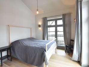 A bedroom with a bed, a nightstand, a chair, a window with curtains, and a wall-mounted light fixture. - Geraumige Wohnung in Detershagen mit Terrasse (Kroepelin)