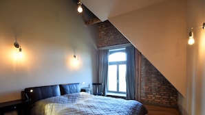 Une chambre avec un grand lit, un mur en briques, une fenêtre avec des rideaux et un plafond en pente.