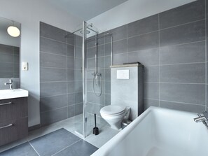 A modern bathroom with a glass-enclosed shower, a white bathtub, and a toilet. - Geraumige Wohnung in Detershagen mit Terrasse (Kroepelin)