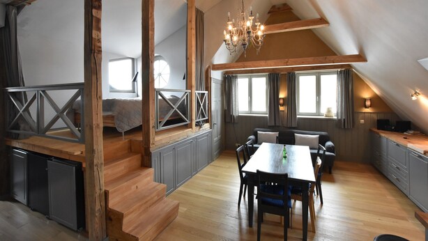 An attic bedroom with a wooden staircase, a dining area with a table and chairs, and a chandelier. - Apartment in Detershagen With Terrace (Kroepelin)