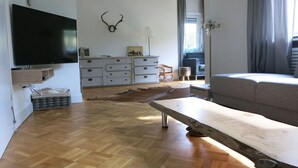 Un soggiorno moderno con pavimento in legno, TV a parete, divano, tavolo da pranzo e un corno di cervo decorativo.
