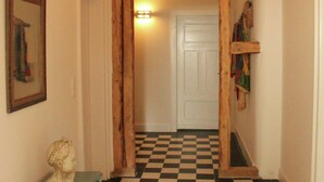 Un corridoio con pavimento a scacchi, una porta bianca e travi in legno a vista.