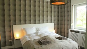 Un letto rifatto con un comodo poggiatesta trapuntato, un comodino con una lampada e una finestra con tende.