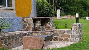A stone patio with a built-in fire pit and seating area, surrounded by a grassy lawn and trees. - Exclusive Apartment in an art Nouveau Villa (Grossschirma)