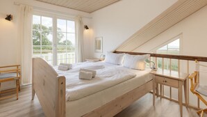 A bedroom with a wooden bed, a desk, and a chair. There is a window with curtains and a view of greenery outside. - Bungalow by the Sea With Sauna in Germany (Sierksdorf)