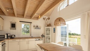 A modern kitchen with white cabinets, a wooden countertop, and a dining area with a wooden table and chairs. - Bungalow by the Sea With Sauna in Germany (Sierksdorf)