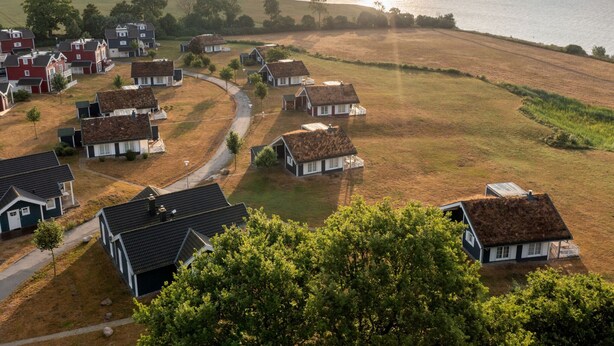 Un village côtier aux maisons aux toits de chaume, avec une route sinueuse et une vue sur la mer.