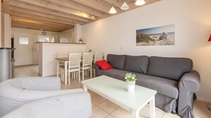 Un salon moderne avec un canapé gris, une table basse blanche et un coin repas avec des chaises blanches.