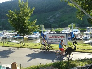 A signboard with text welcoming visitors to a location, a body of water with boats, and a cyclist on the road.