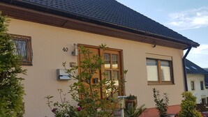 A building with a beige exterior, a wooden door, and a window with a number '40' above it. There are potted plants and a small garden area in front of the building. - Modern Holiday Apartment With Large Garden Near the River Moselle (Neumagen-Dhron)