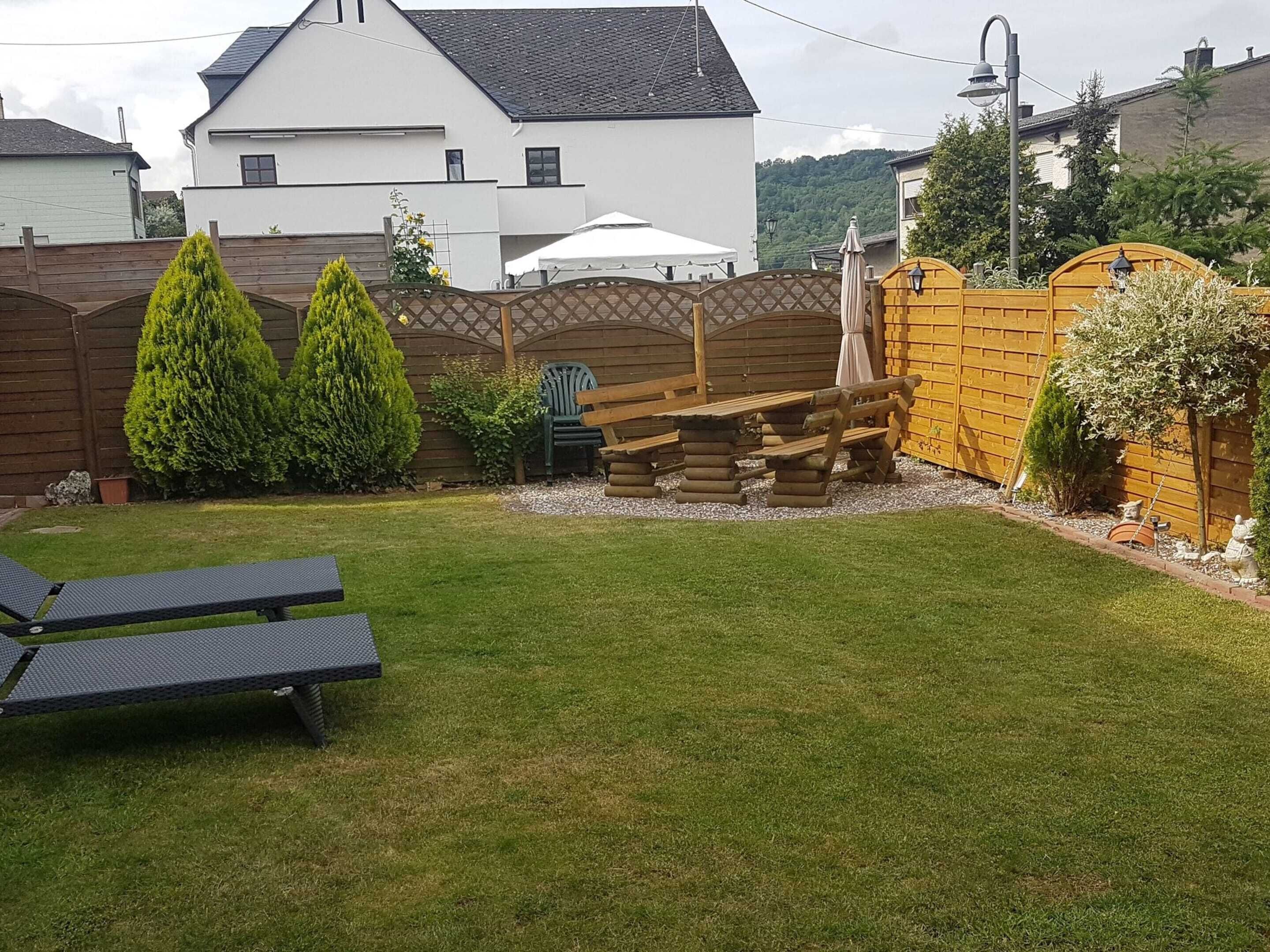 A backyard with a wooden bench, a small table, and a lawn.