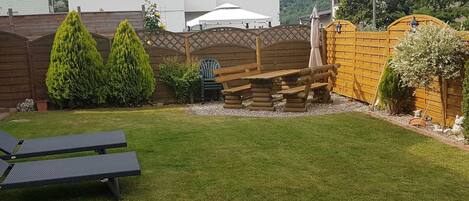 A backyard with a wooden bench, a small table, and a lawn.