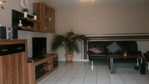 A modern living room with a flat-screen TV, wooden cabinets, a large potted plant, and a black leather sofa. - Modern Holiday Apartment With Large Garden Near the River Moselle (Neumagen-Dhron)