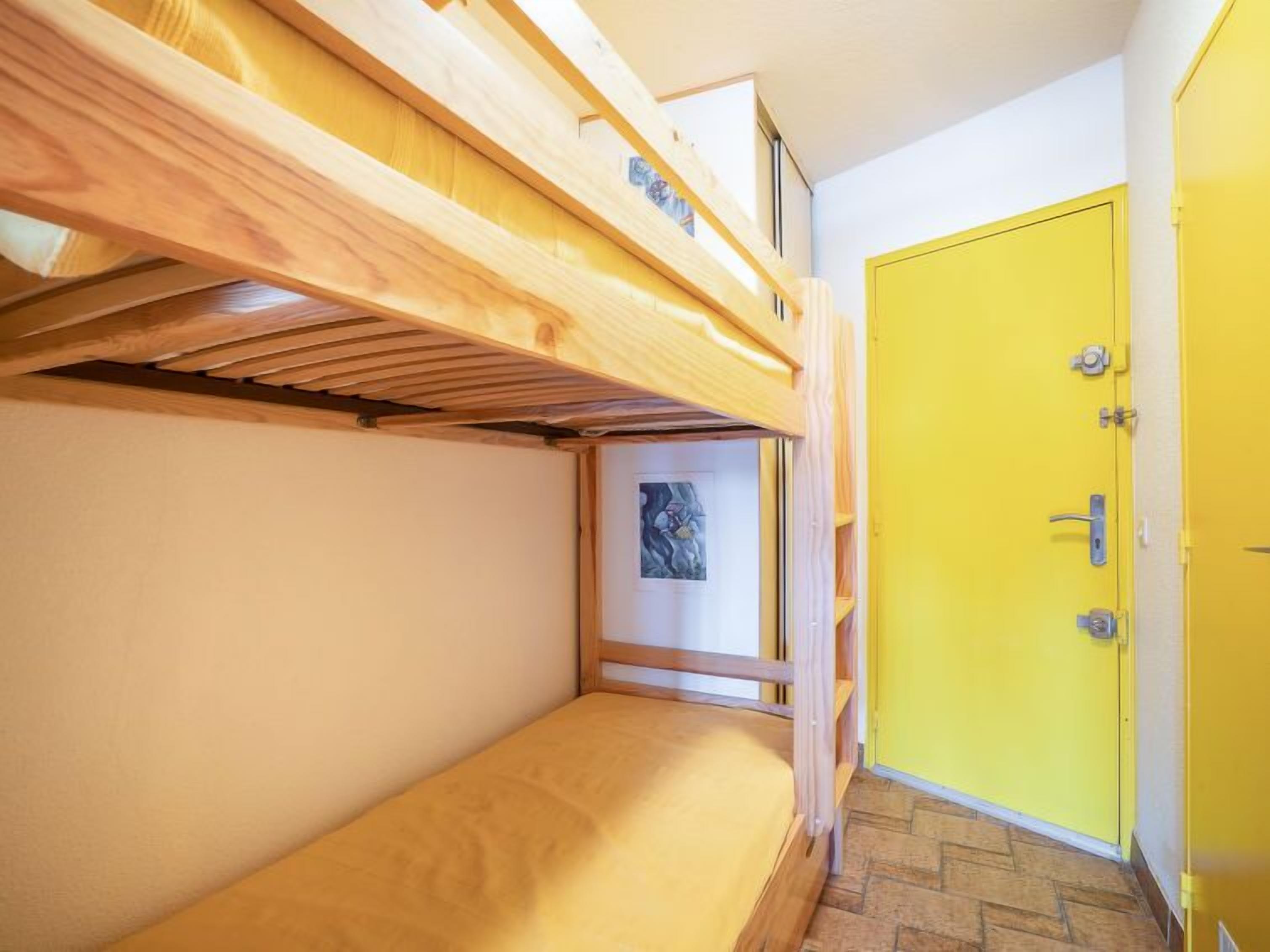 Une chambre avec des lits superposés, une porte jaune et un tableau encadré au mur.