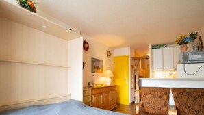 A room with a bed, a small desk, a chair, and a kitchenette. - La Croisière by Interhome (Port Camargue)