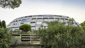A large, dome-shaped building with a grid-like facade, surrounded by greenery and a stone pathway leading to a gate. - La Croisière by Interhome (Port Camargue)