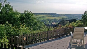Ein Holzzaun im Vordergrund mit einem Stuhl, mit Blick auf eine ländliche Landschaft mit Feldern und Häusern.