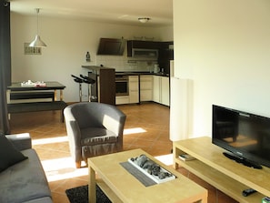A living room with a sofa, a coffee table, a TV, and a kitchen area in the background. - Modernes Apartment mit Zentralheizung in Willingen (Willingen)
