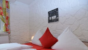 A bed with white and red bedding, a red pillow, and a wall-mounted sign.