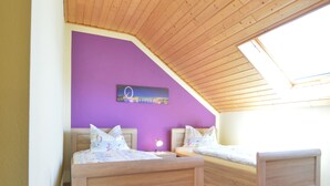 A bedroom with two wooden beds, a purple wall, and a skylight.