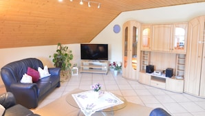 A living room with a wooden ceiling, a leather sofa, a TV, a coffee table, and built-in wooden cabinets.