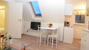 Un espacio habitable compacto con comedor, una kitchenette y un televisor pequeño montado en la pared.