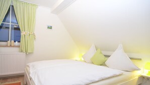 Un dormitorio con una cama individual, una ventana con cortinas, una mesita de noche con lámpara y un radiador.