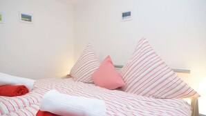 Una cama bien hecha con ropa de cama a rayas y una almohada roja, toallas blancas y un pequeño cuadro en la pared.